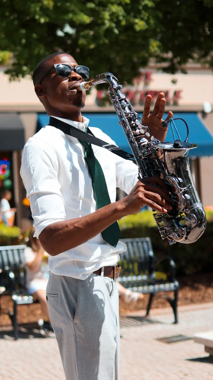 Saxophonist performing for a community audience outdoors in a park